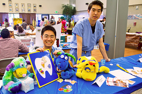 two individuals wearing doctors' scrubs holding stuffed animals and a picture of a tooth