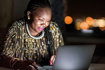 A Black woman and business owner works on her computer at night.