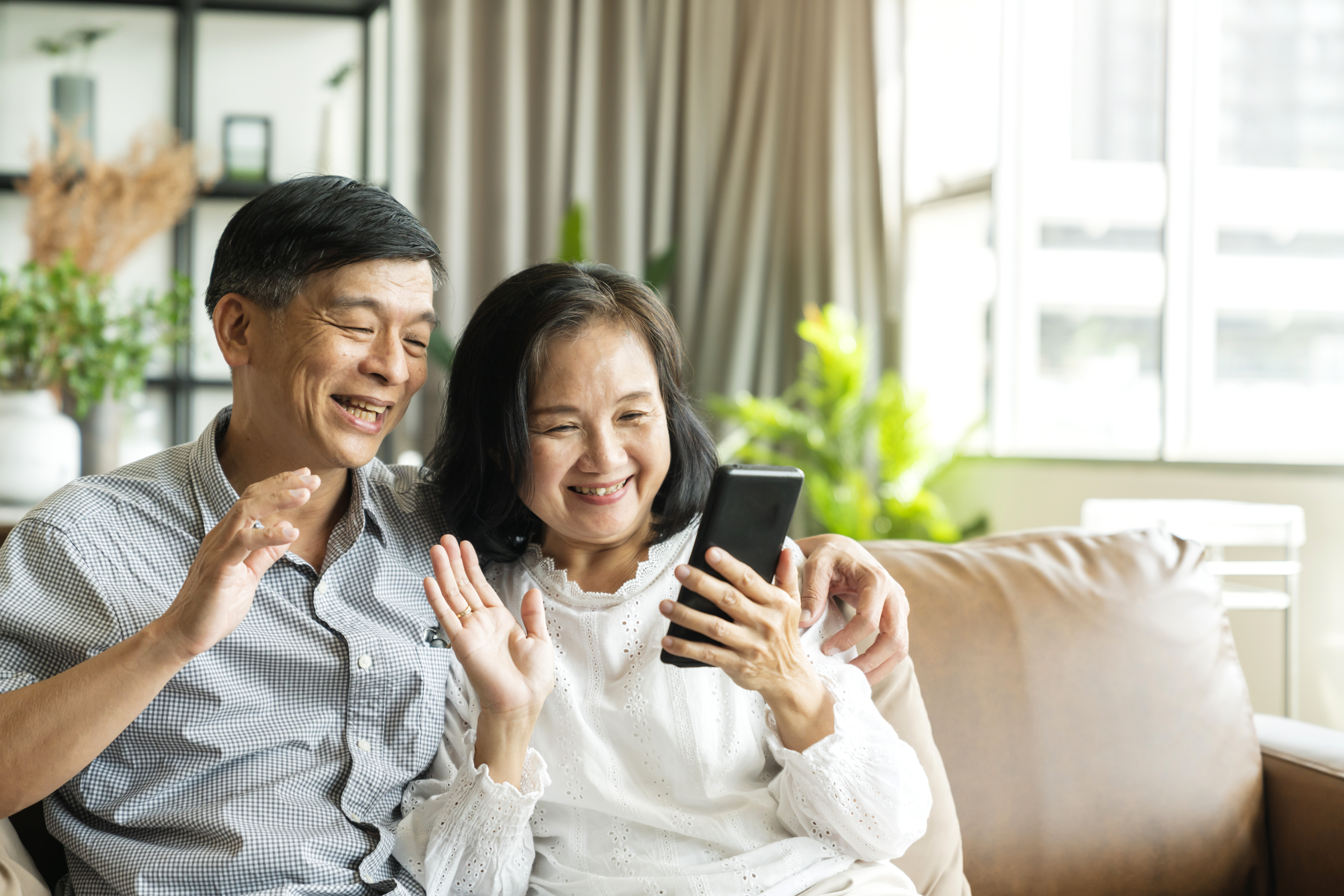 Couple waving while holding up cell phone.