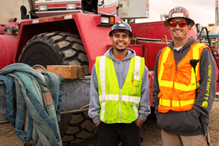 two vested workers standing shoulder to shoulder in front of a tractor