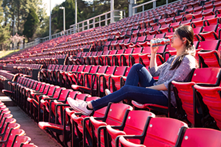 woman sitting alone in stadium seating drinking from water bottle