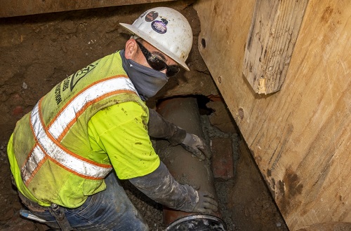 worker in a trench holding a sewer lateral