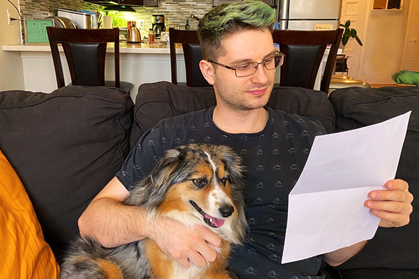 person reading a paper and sitting with their dog on the couch