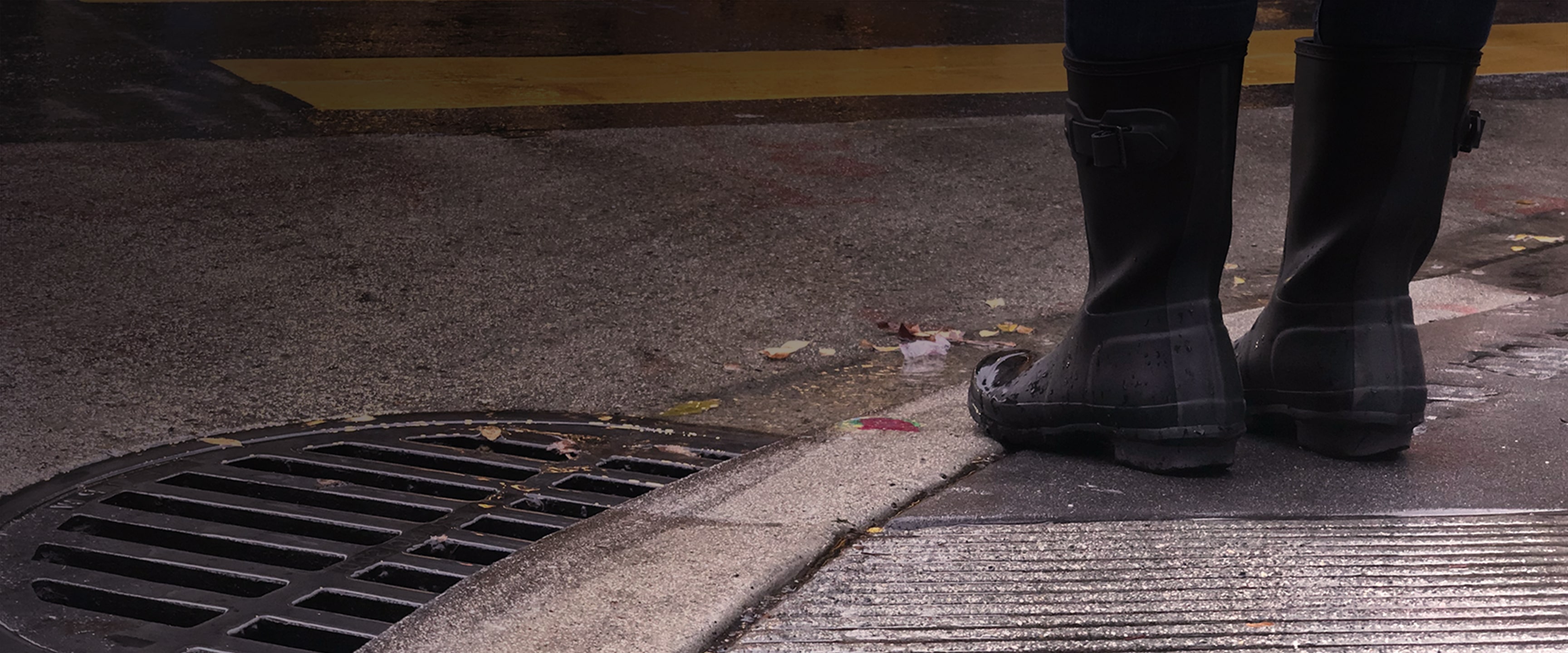 rain boots standing at curb by the sewer drain