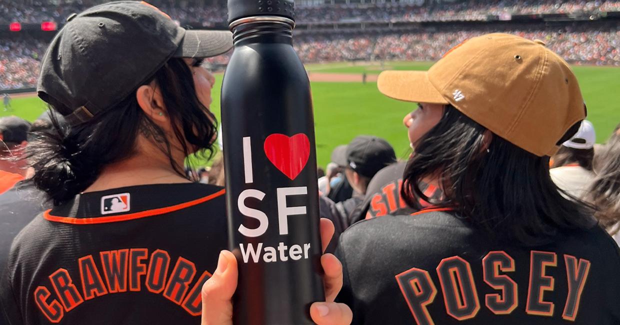 Two people holding an I love SF Water water bottle at SF Giants game